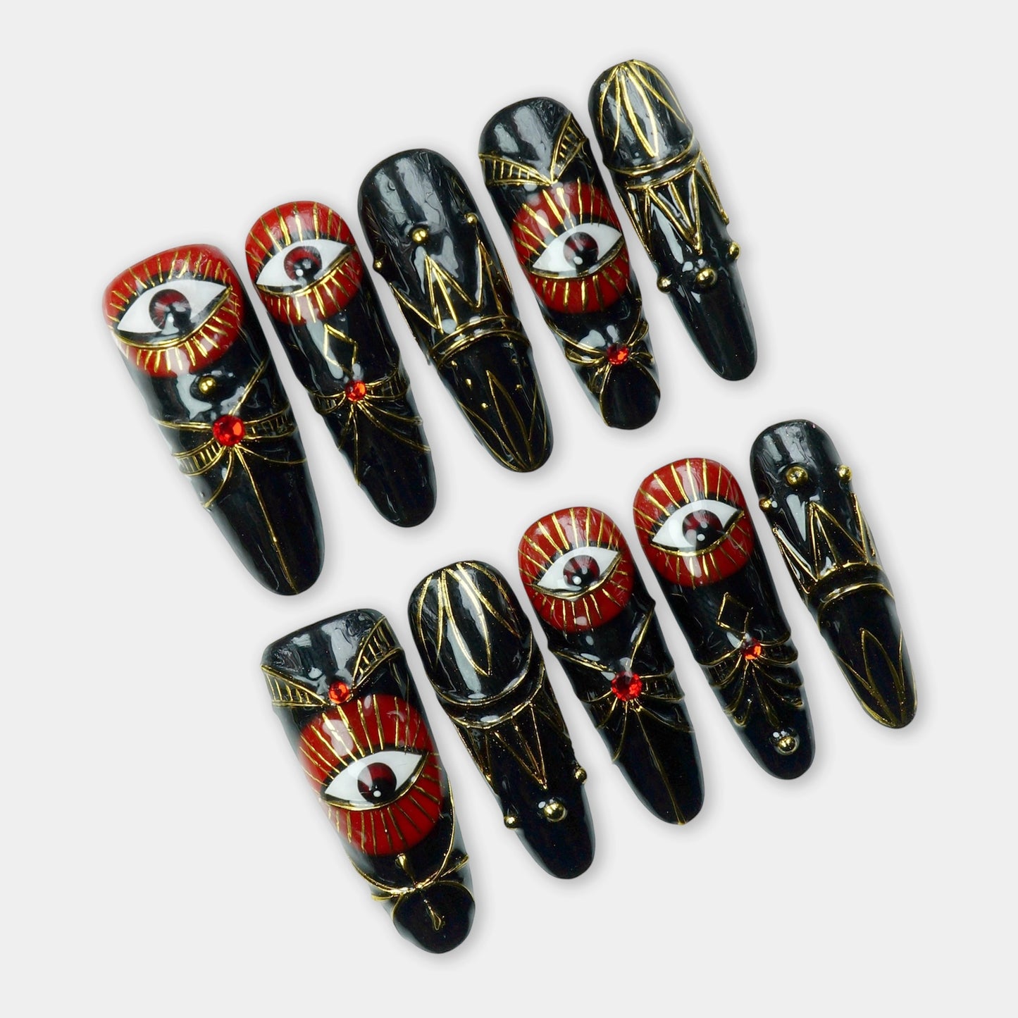 Striking black press-on nails with red evil eye designs, gold details, and gemstone accents – a powerful statement set by Donailsart