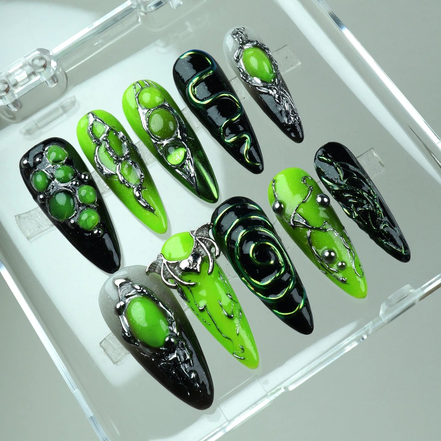 Alien-core press-on nails with glowing green polish, silver sculpted frames, and otherworldly motifs
