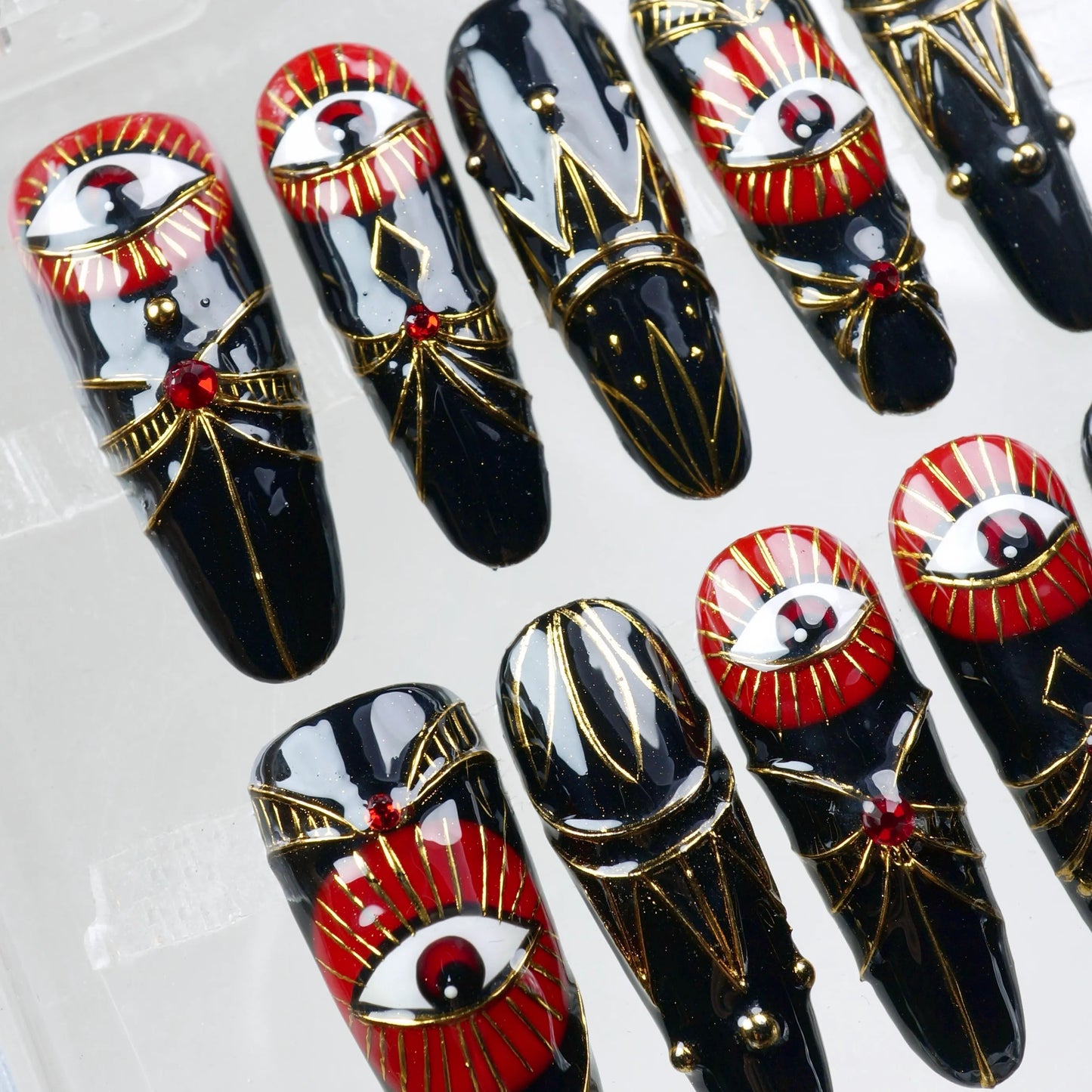 Glossy black press-on nails with red all-seeing eye and gold ornamental lines