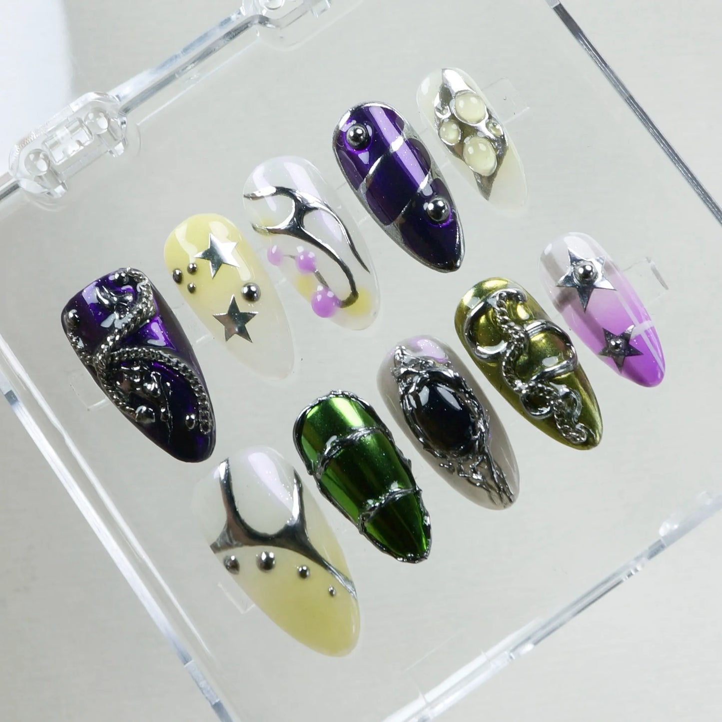 Bold, mismatched chrome nails with alien-core vibes—think stars, metallic chains, jelly drops, and cosmic shine.