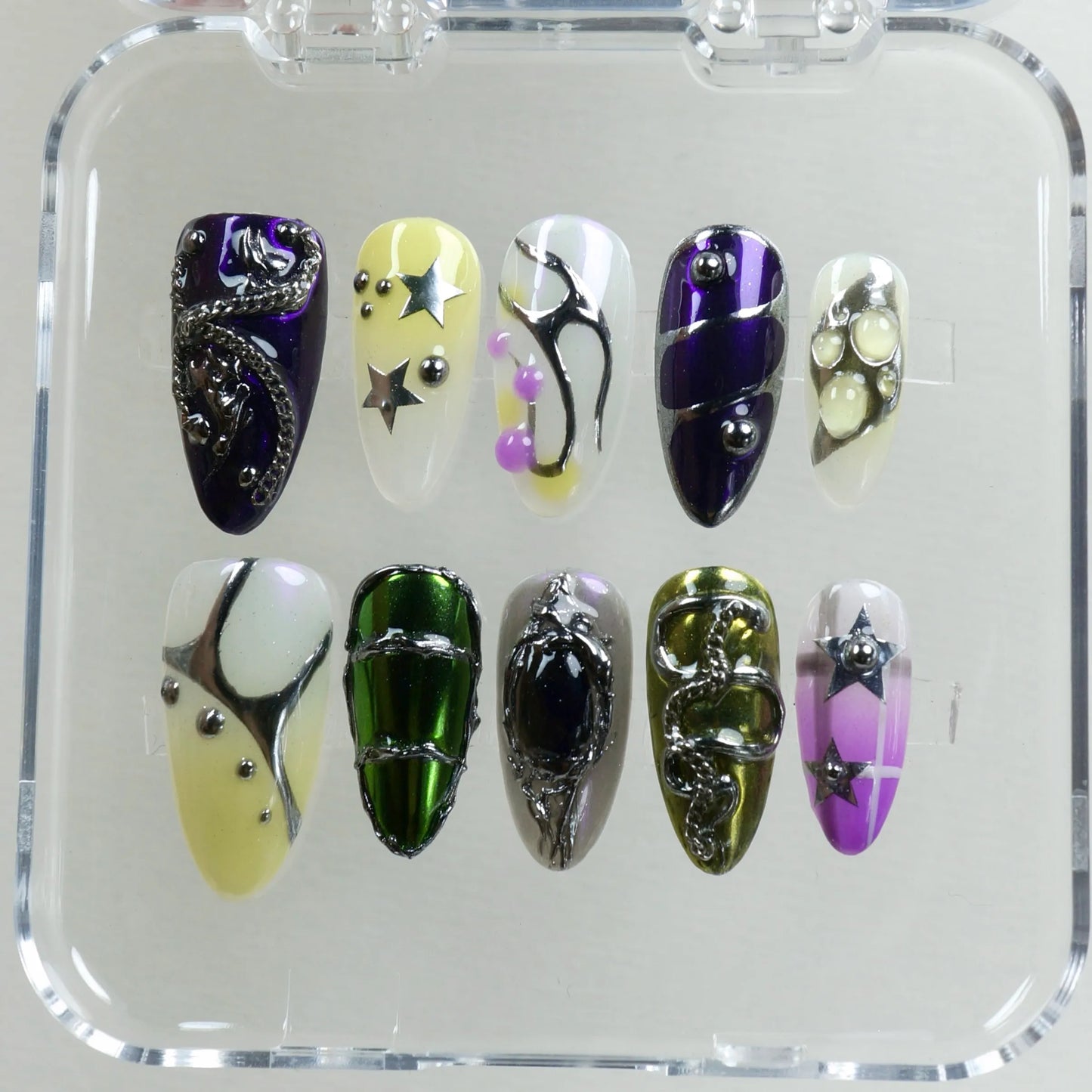 Colorful press-on nails with star charms, chrome green and purple accents, Y2K aesthetic, and metallic 3D nail art.