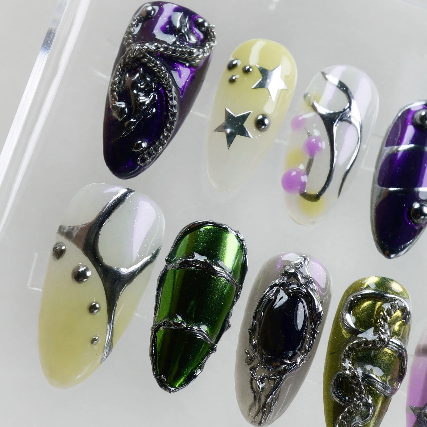 Colorful press-on nails with star charms, chrome green and purple accents, Y2K aesthetic, and metallic 3D nail art.