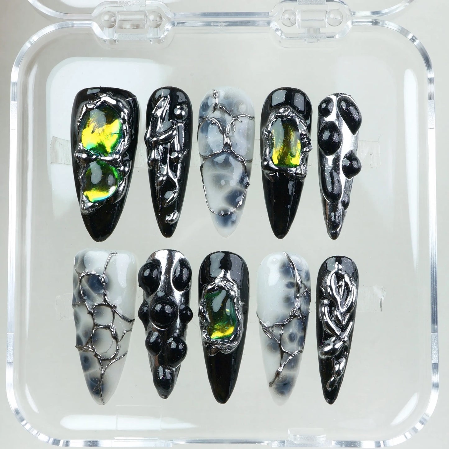 Black and smoky translucent press-on nails featuring chrome webbing, iridescent yellow-green gem accents, and 3D droplet textures.