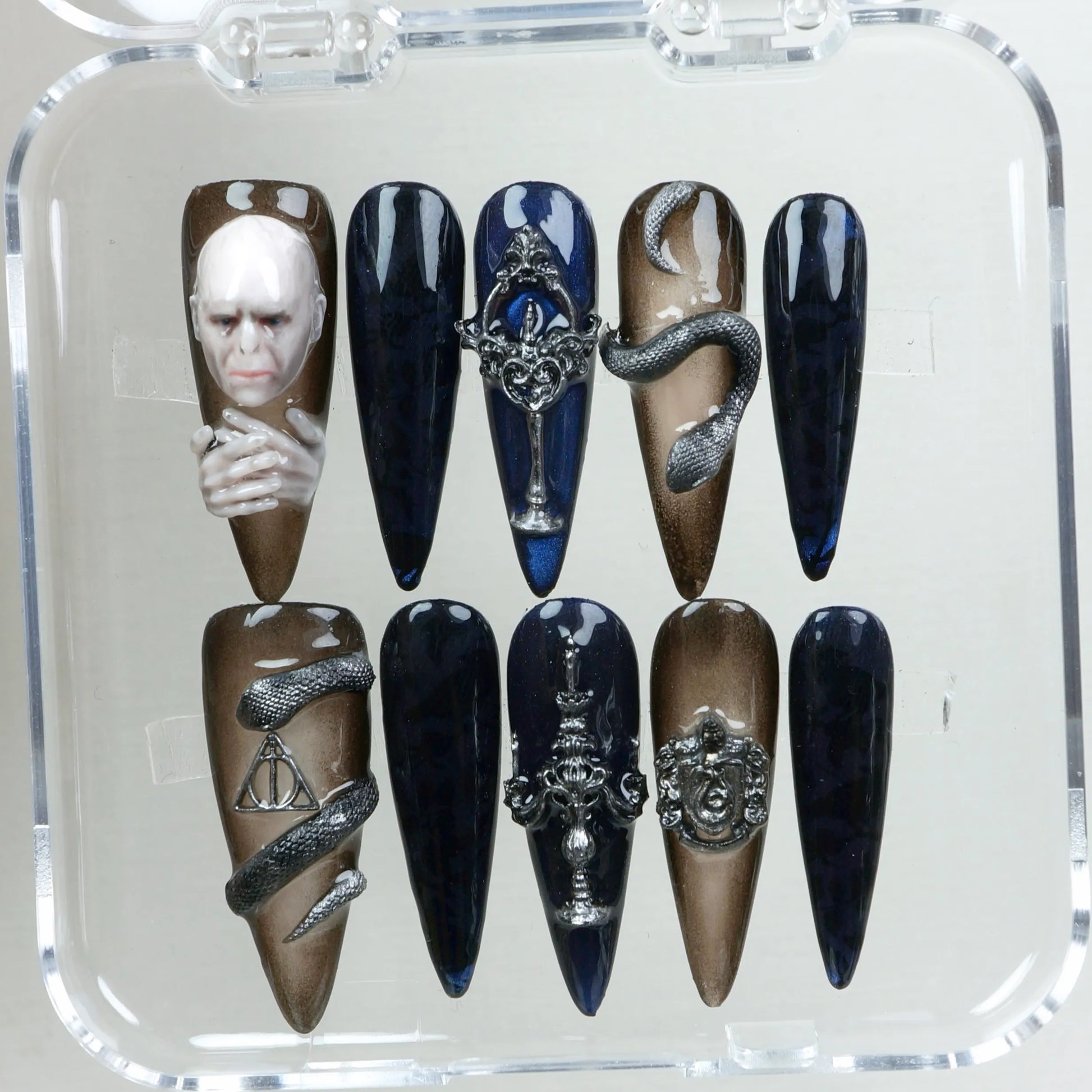 Custom nail art set with 3D elements, including a sculpted face, snake wrap, and ornate silver charms