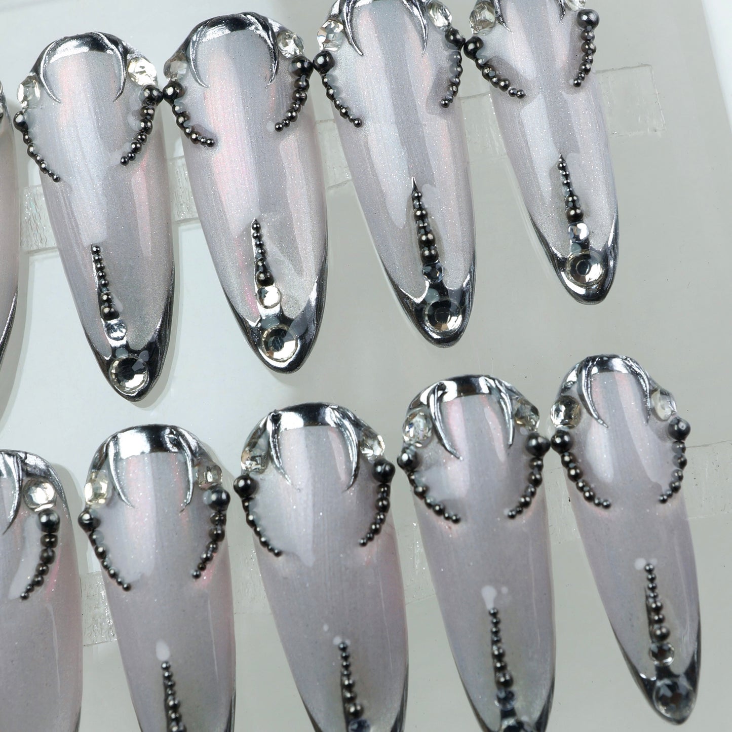 Sharp and sleek, these metallic press-on nails feature dark chrome edges and beadwork like a digital lace tattoo.