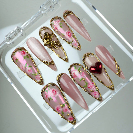 Romantic rose-themed press-on nails with vintage gold frames, angel charm, and heart accent on a nude base.