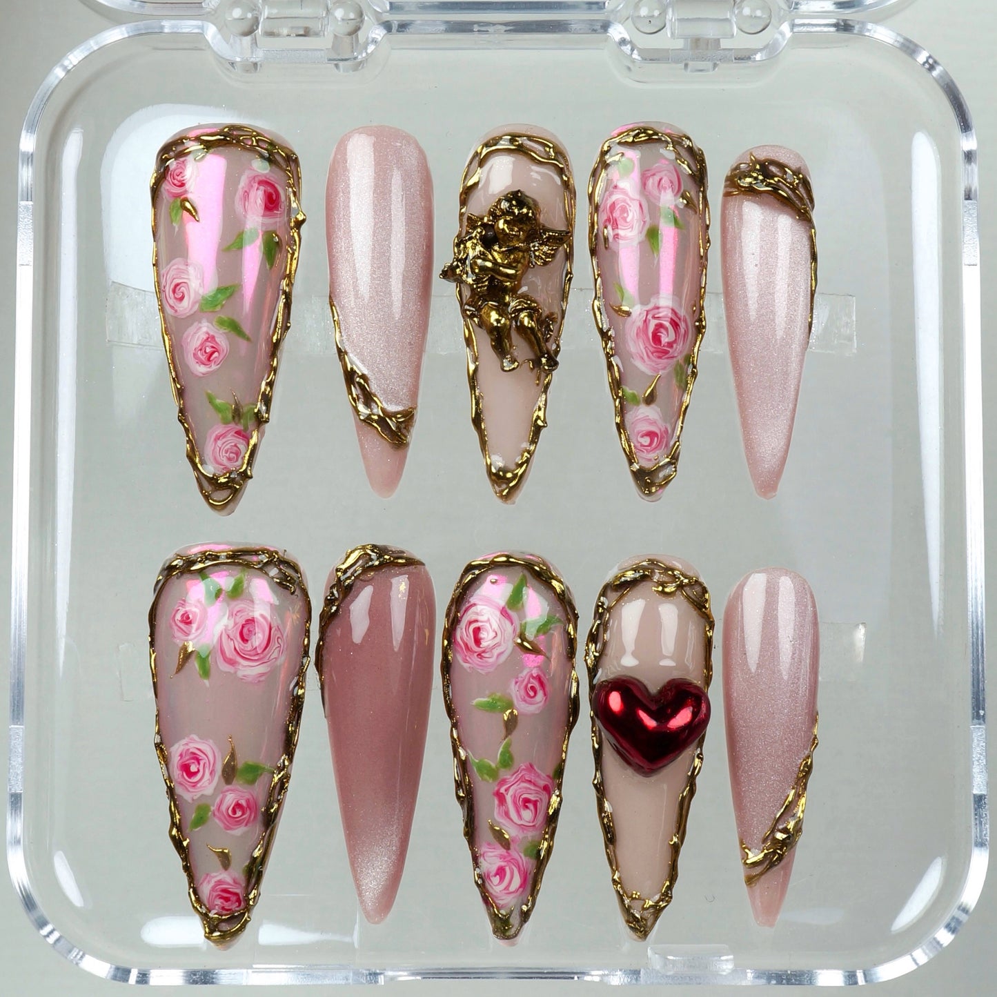Victorian-inspired press-on nails featuring delicate floral patterns, baroque gold trim, and a love-struck cherub.