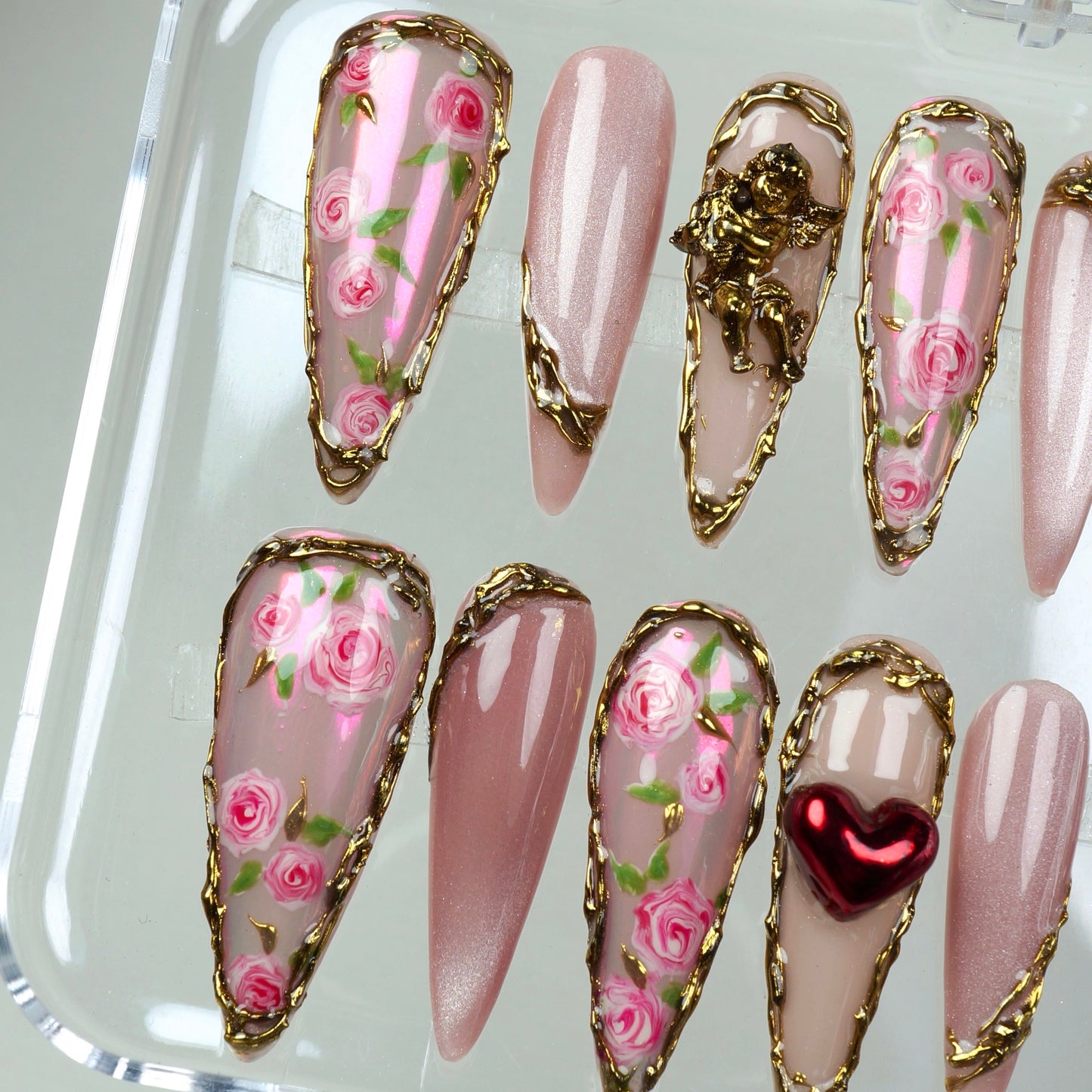 Victorian-inspired press-on nails featuring delicate floral patterns, baroque gold trim, and a love-struck cherub.