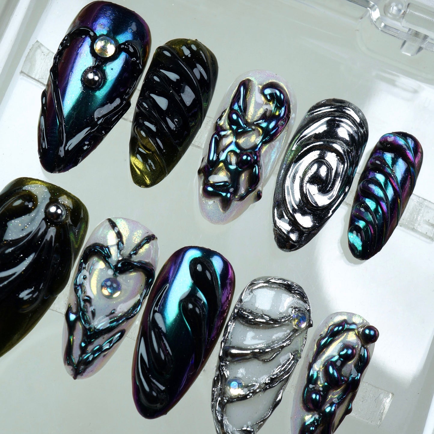 Iridescent press-on nails with sculpted black chrome designs and silver 3D detailing – a bold, high-fashion nail art look.