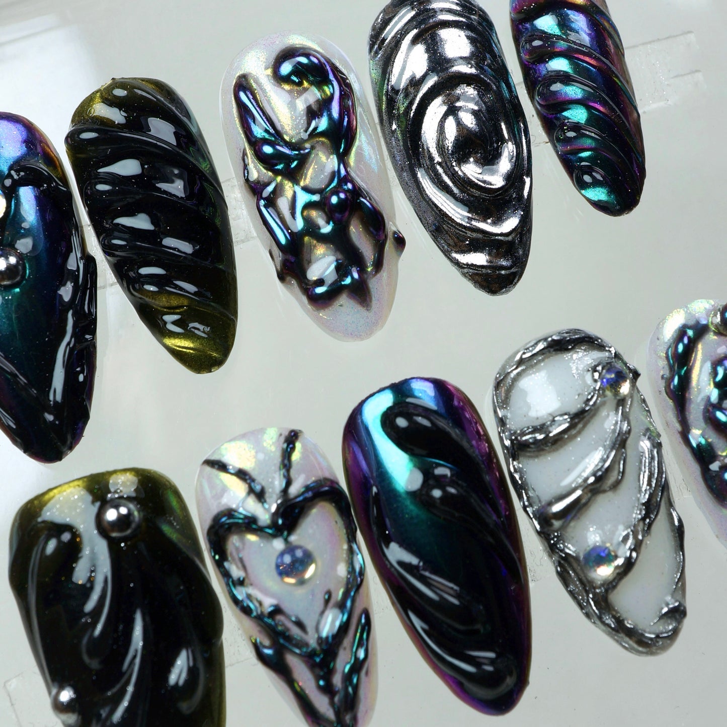 Iridescent press-on nails with sculpted black chrome designs and silver 3D detailing – a bold, high-fashion nail art look.