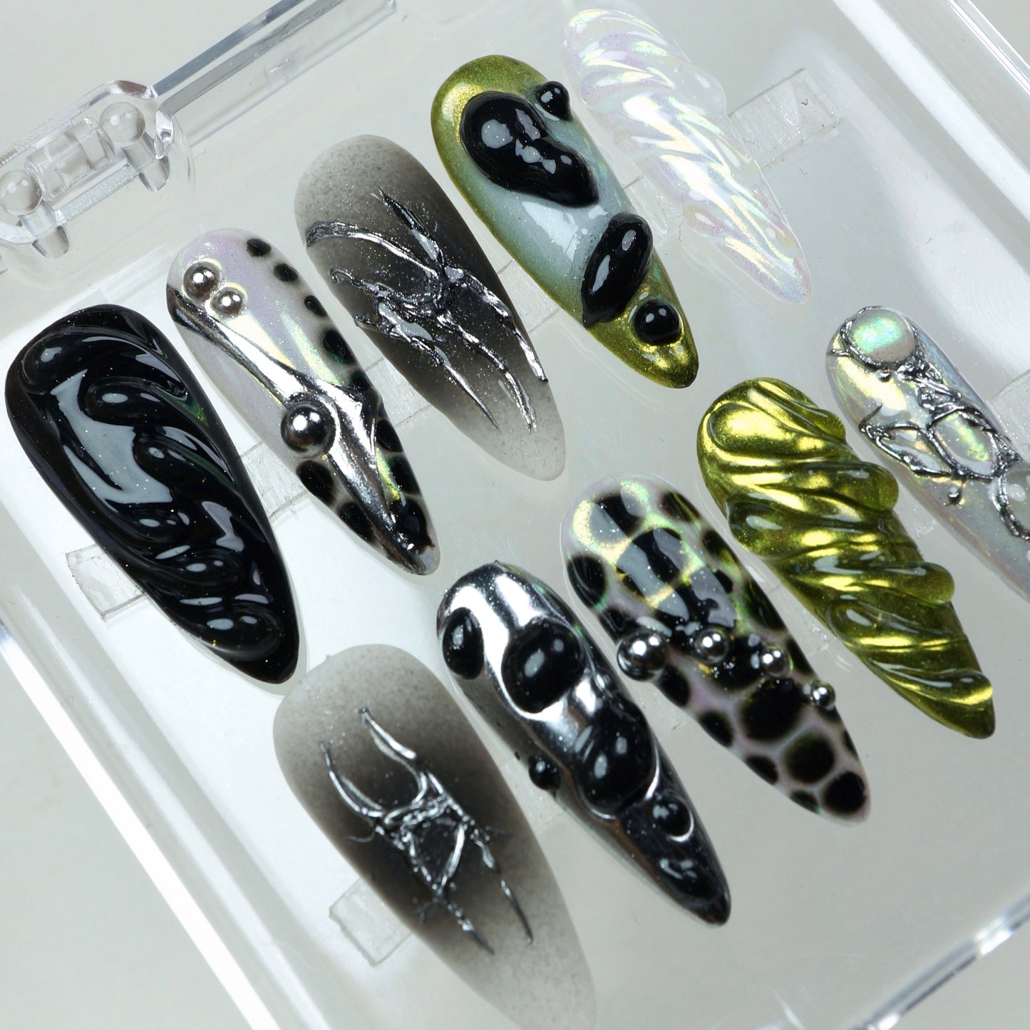Press-on nails with holographic shine, black jelly swirls, metallic green chrome, and bold 3D textures.