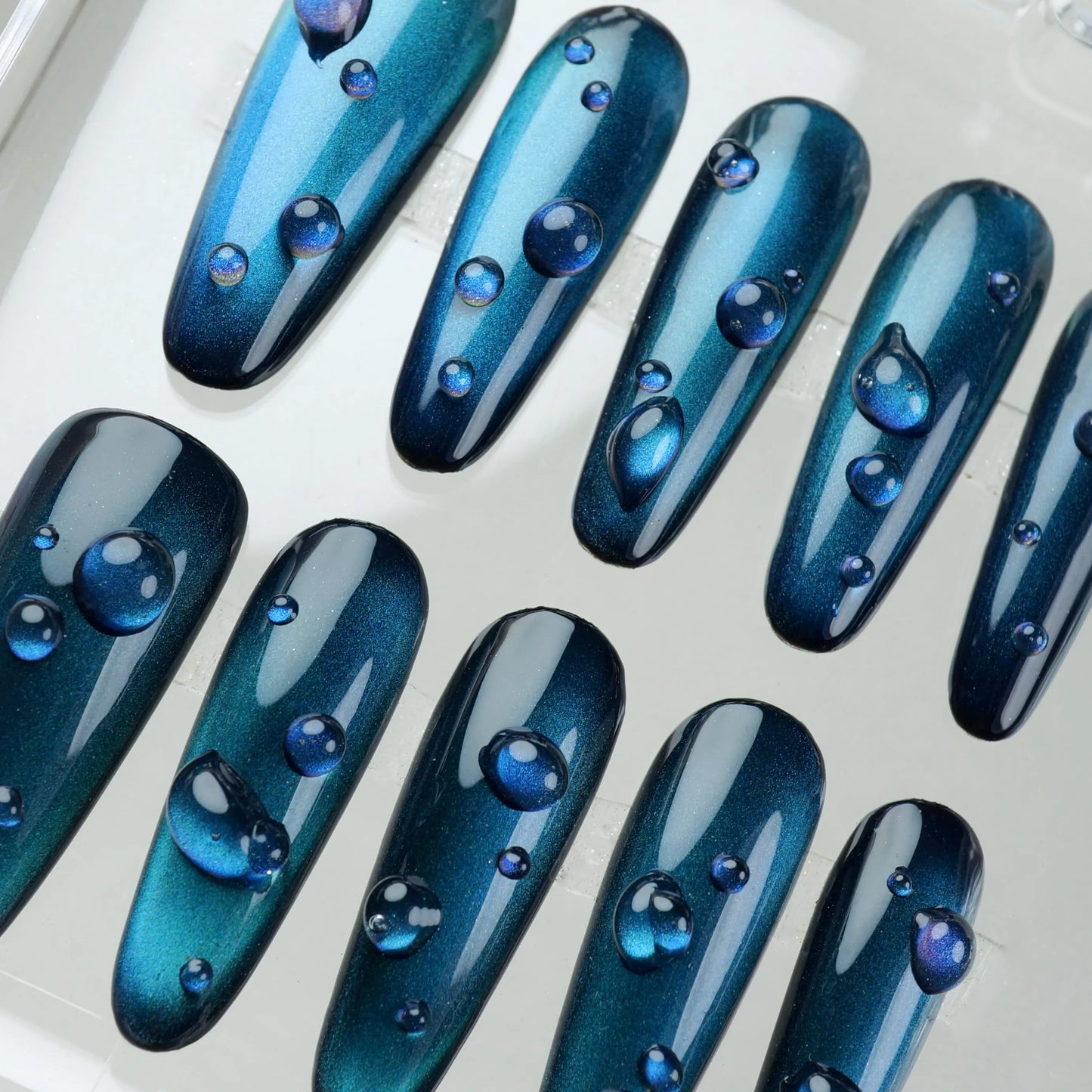 Cat eye gel nails with hypnotic teal-blue reflections and crystal-clear droplet effects, by Donailsart