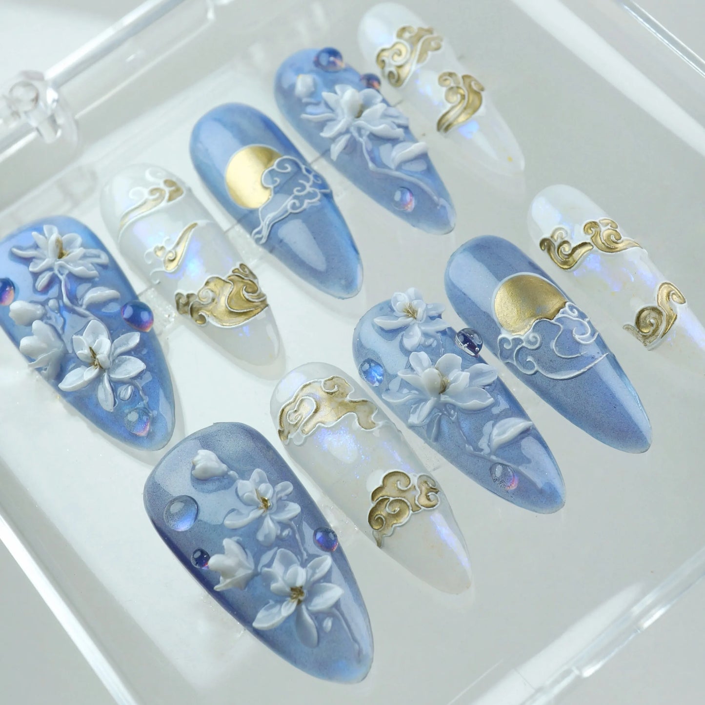 Dreamy press-on nails featuring moonlit skies, flowing gold clouds, and 3D white blossoms on a misty blue and opal base