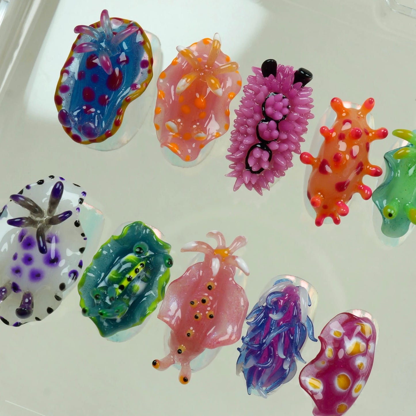 Sea Slug Color full press-on nail set fanned out outside case displaying all 10 vibrant nudibranch designs including blue, purple spiky, orange, green, white spotted, teal, pink, blue-purple swirl, and hot pink sea slug nails