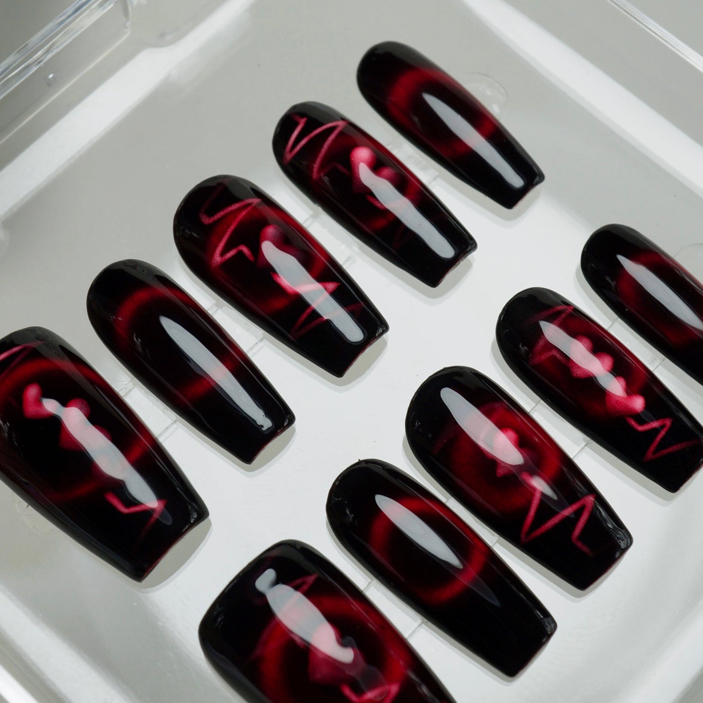 Black and red nail art designs on press-on nails in a white tray.