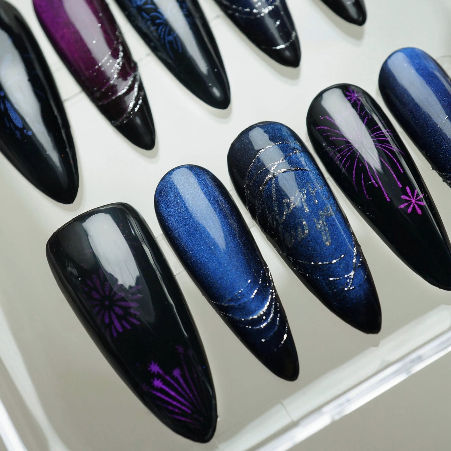 Almond-shaped cat-eye nails in black, blue, and purple with sparkling firework art.