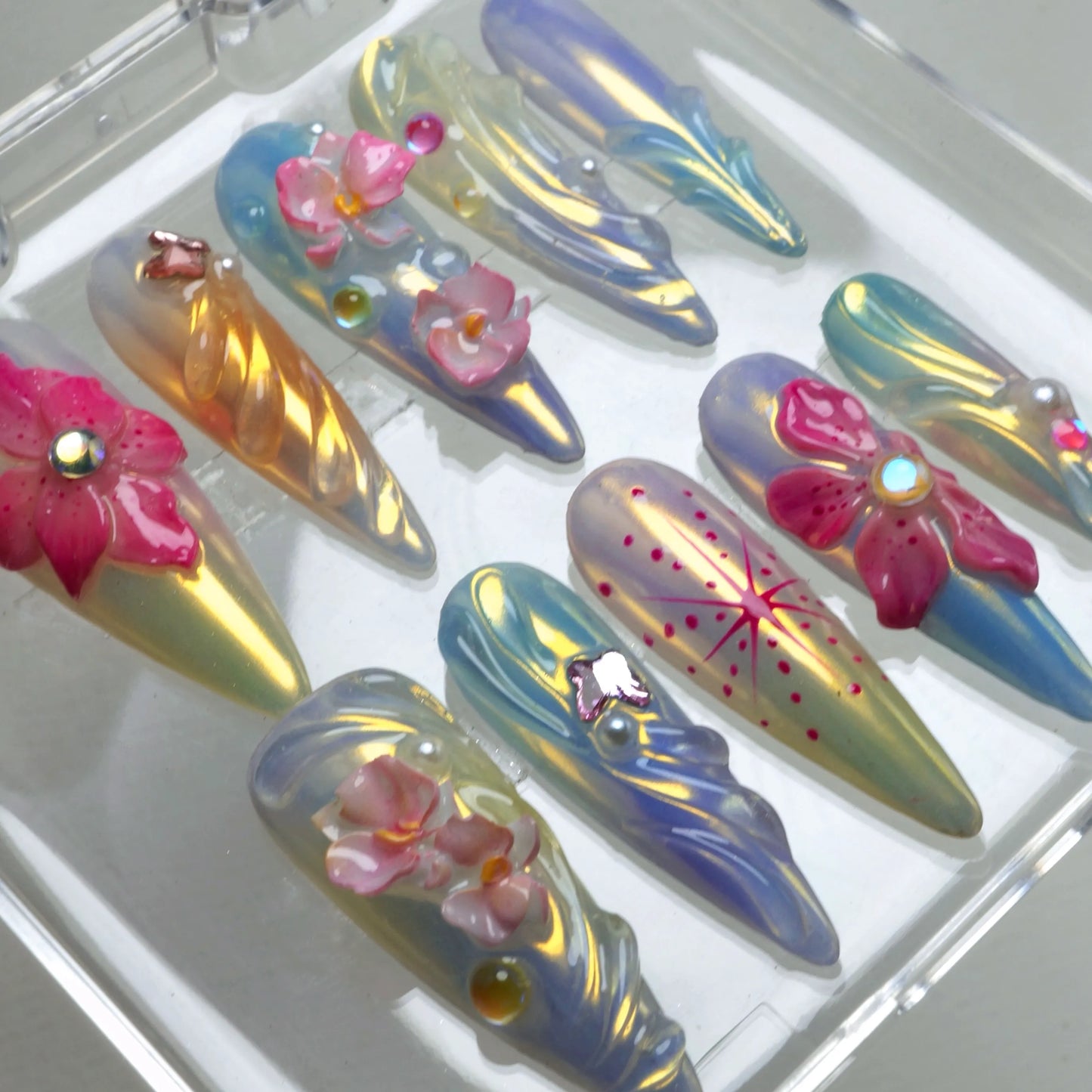 Summer flower nails in pastel yellow and blue hues with butterfly charms, starburst details, and crystal florals