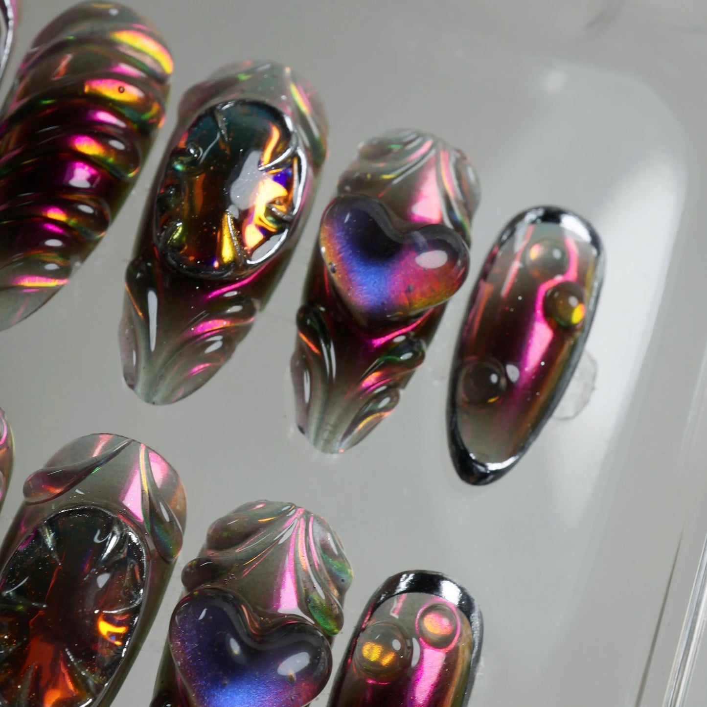 Futuristic press-on nails from Donailsart with multidimensional 3D designs, reflective heart motifs, and gemstone-inspired textures