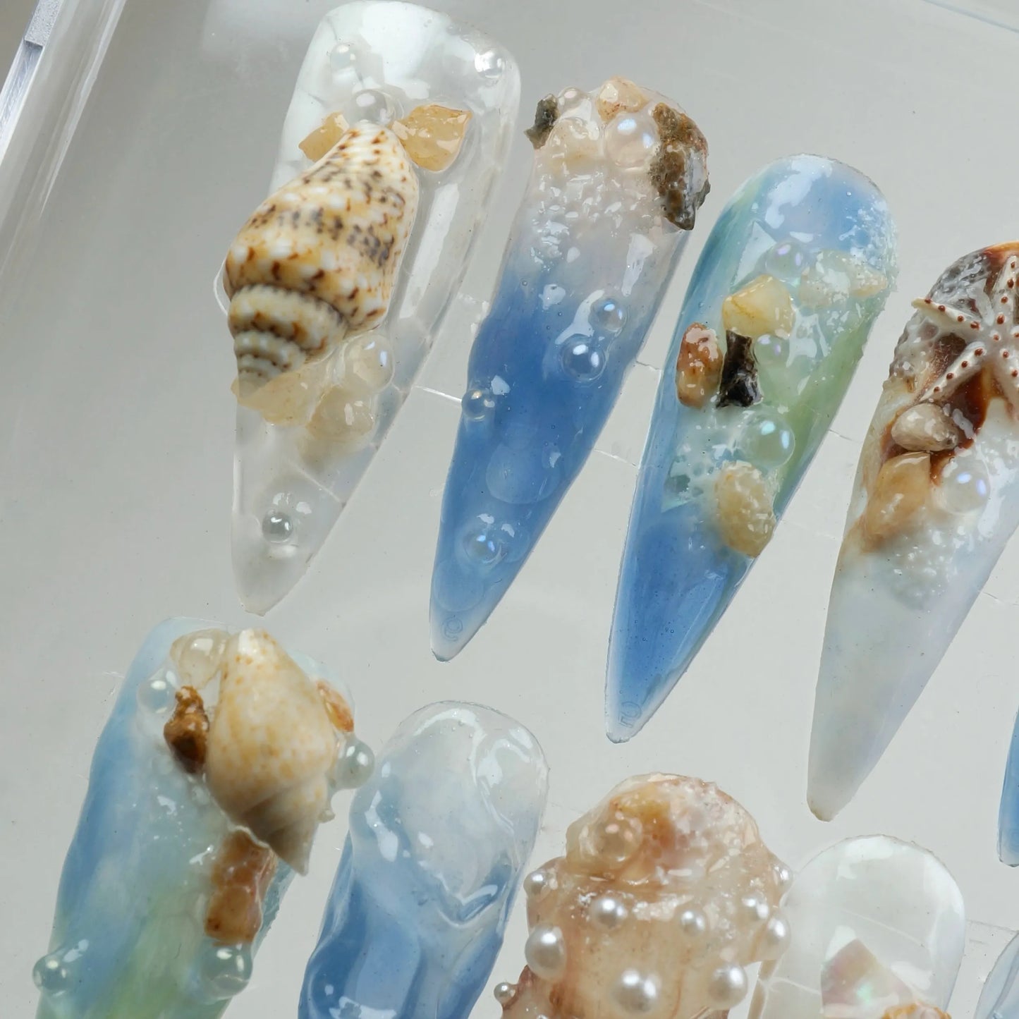 Ocean-inspired nail designs with seashells and blue gradient.