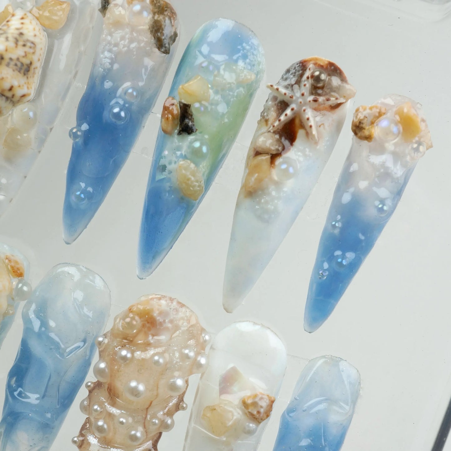 Ocean-inspired nail designs with seashells and blue gradient.