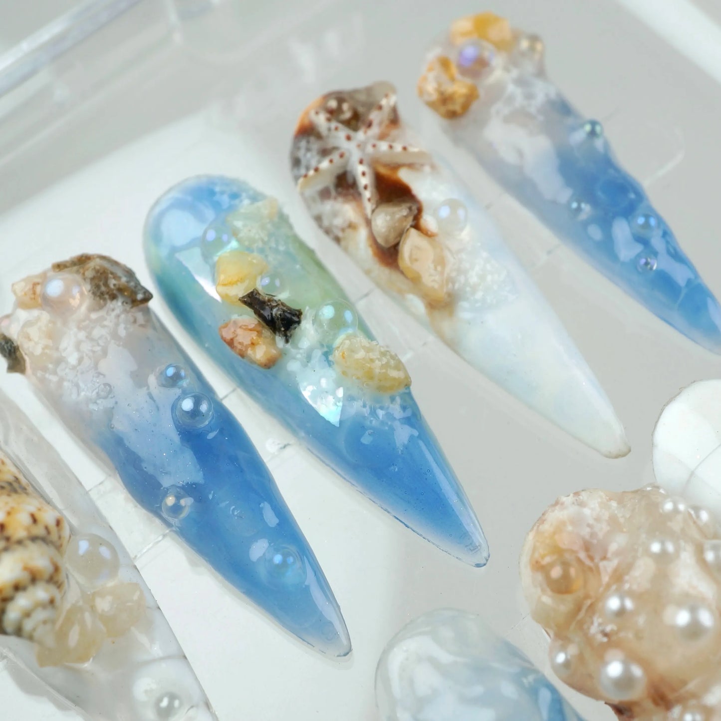Ocean-inspired nail designs with seashells and blue gradient.