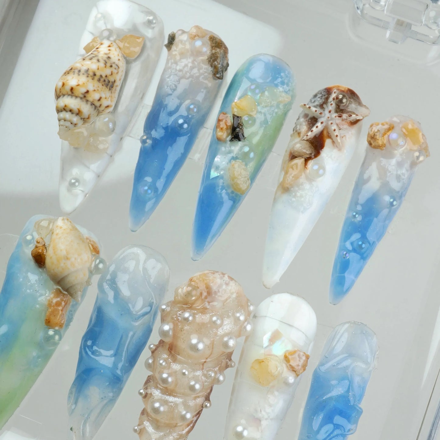 Ocean-inspired nail designs with seashells and blue gradient.
