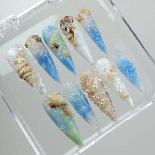 Ocean-inspired nail designs with seashells and blue gradient.