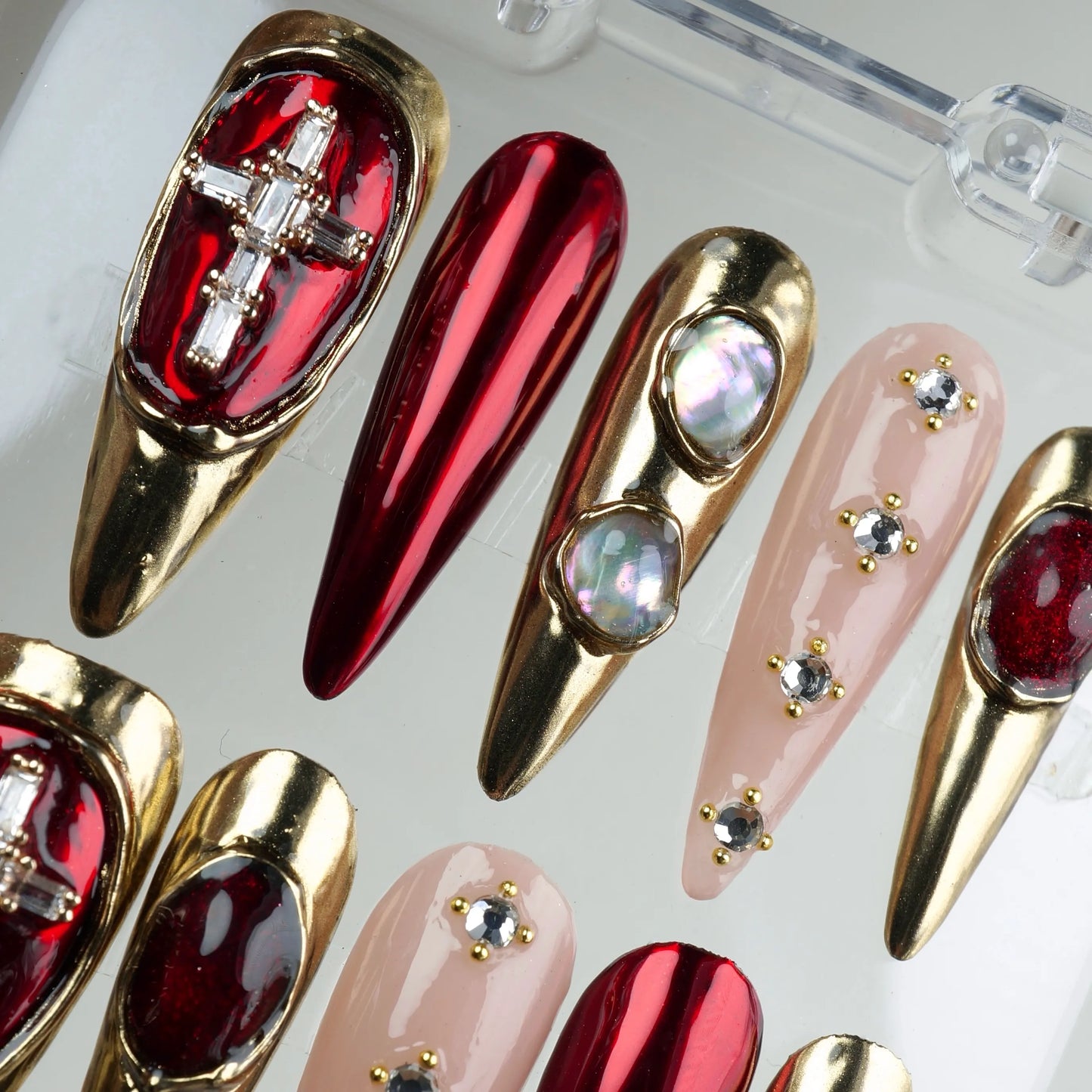 Striking press-on nails with gold and red chrome mix, nude rhinestone nails, and sculptural jewel settings