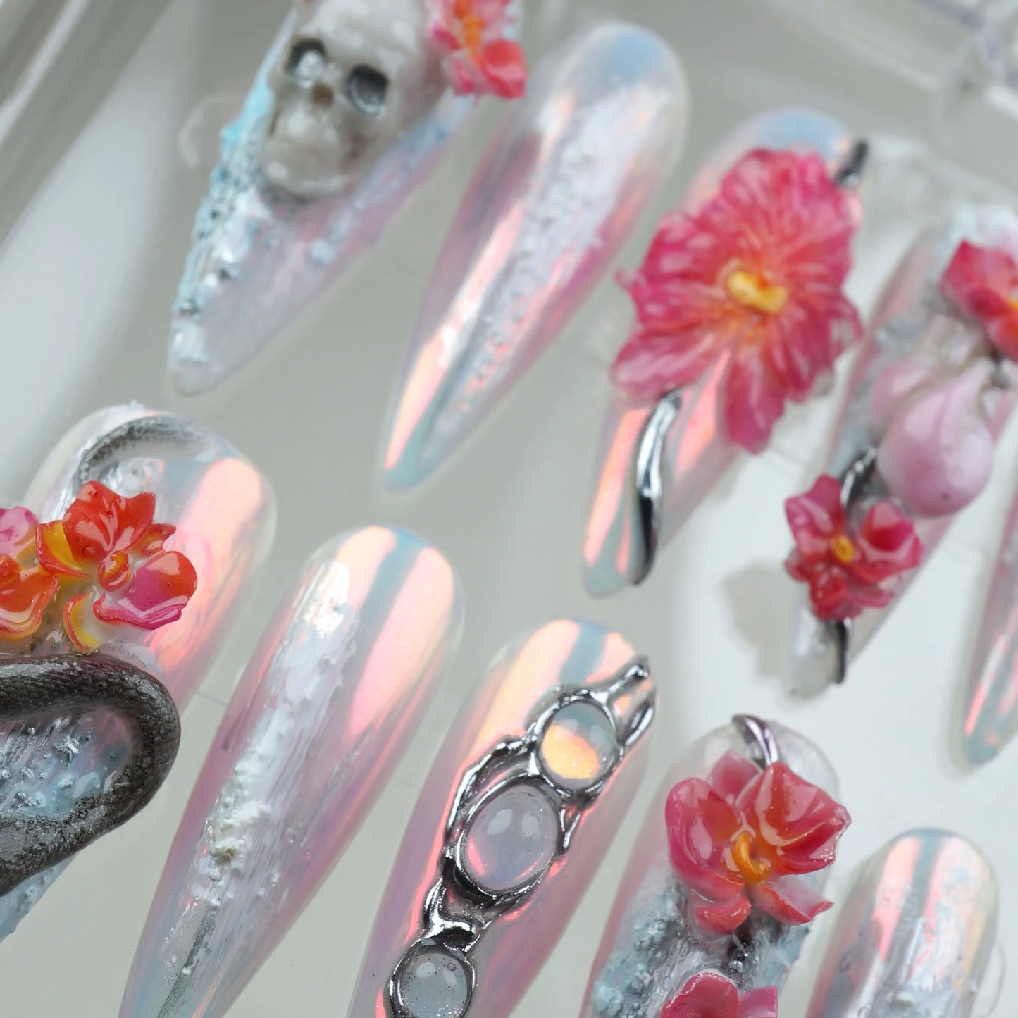 Statement summer nails art with reflective finishes, vibrant pink florals, and 3D gothic accents like bones and snakes