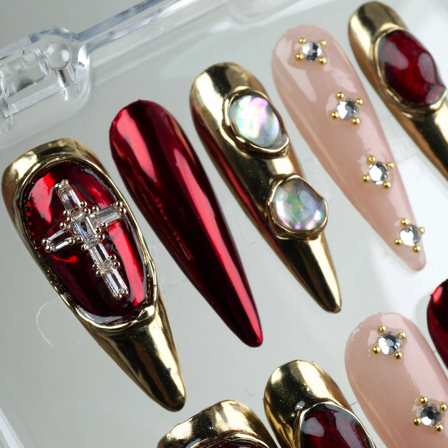 Bold press-on nails from Donailsart with reflective red polish, gold 3D details, and pearl-like stones