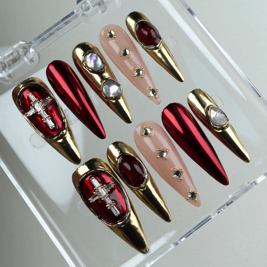 Glamorous press-on nails featuring deep ruby red, gold accents, and cross-shaped crystal charms for a regal finish