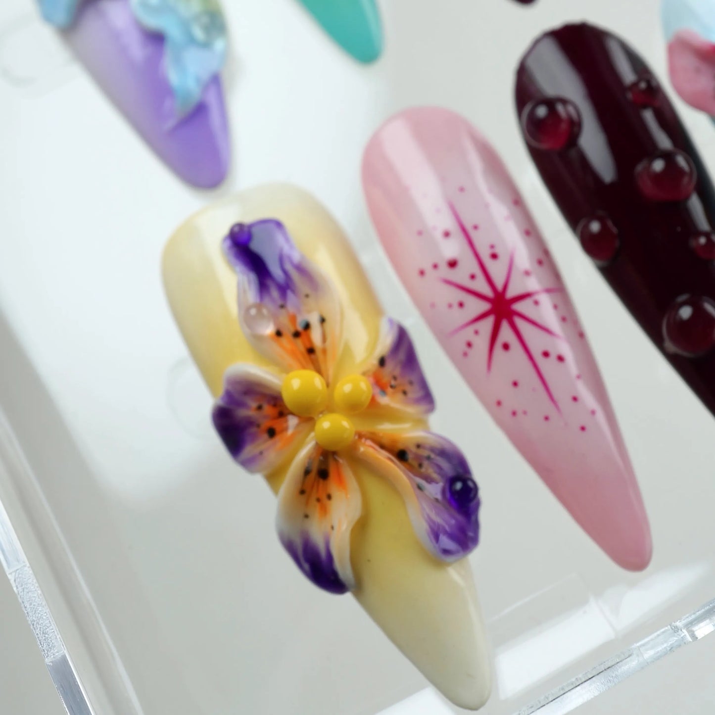 Vibrant press-on nails with bright 3D flowers, dripping dew effects, and sunset-inspired color blends