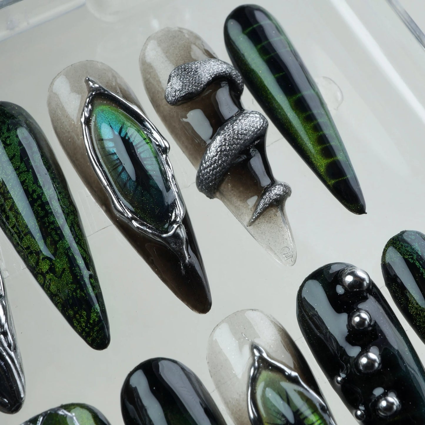 Dark green cat-eye nails design with hexagon scales, sculpted textures, and reflective reptilian elements