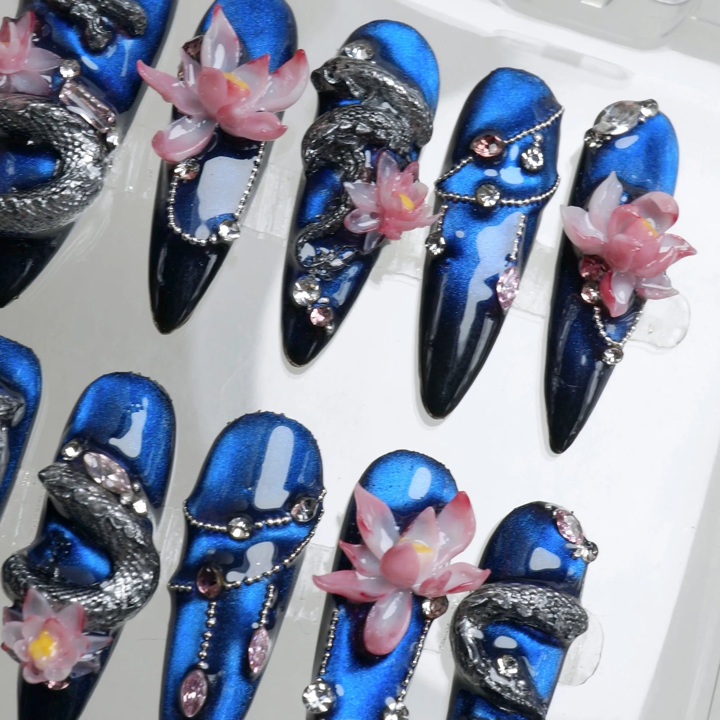 Nails art with fierce dragon motifs, pink lotus flowers, and deep blue galaxy-inspired backgrounds