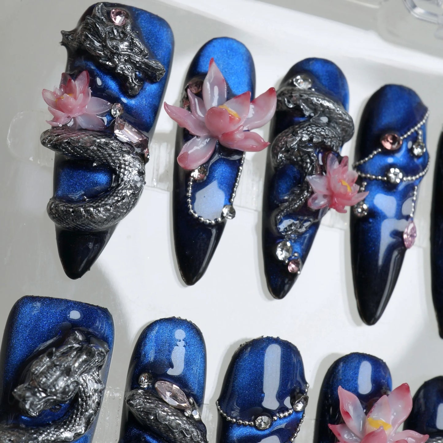 Nails art with fierce dragon motifs, pink lotus flowers, and deep blue galaxy-inspired backgrounds