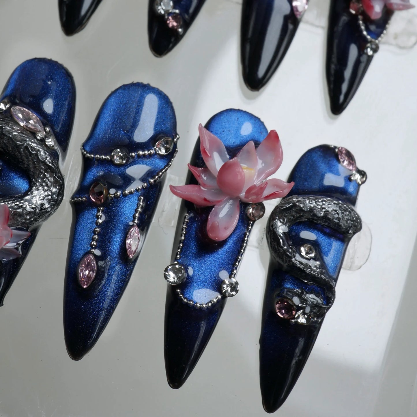 Bold nails art with detailed dragon sculptures, pink floral accents, and glossy black and blue gradients