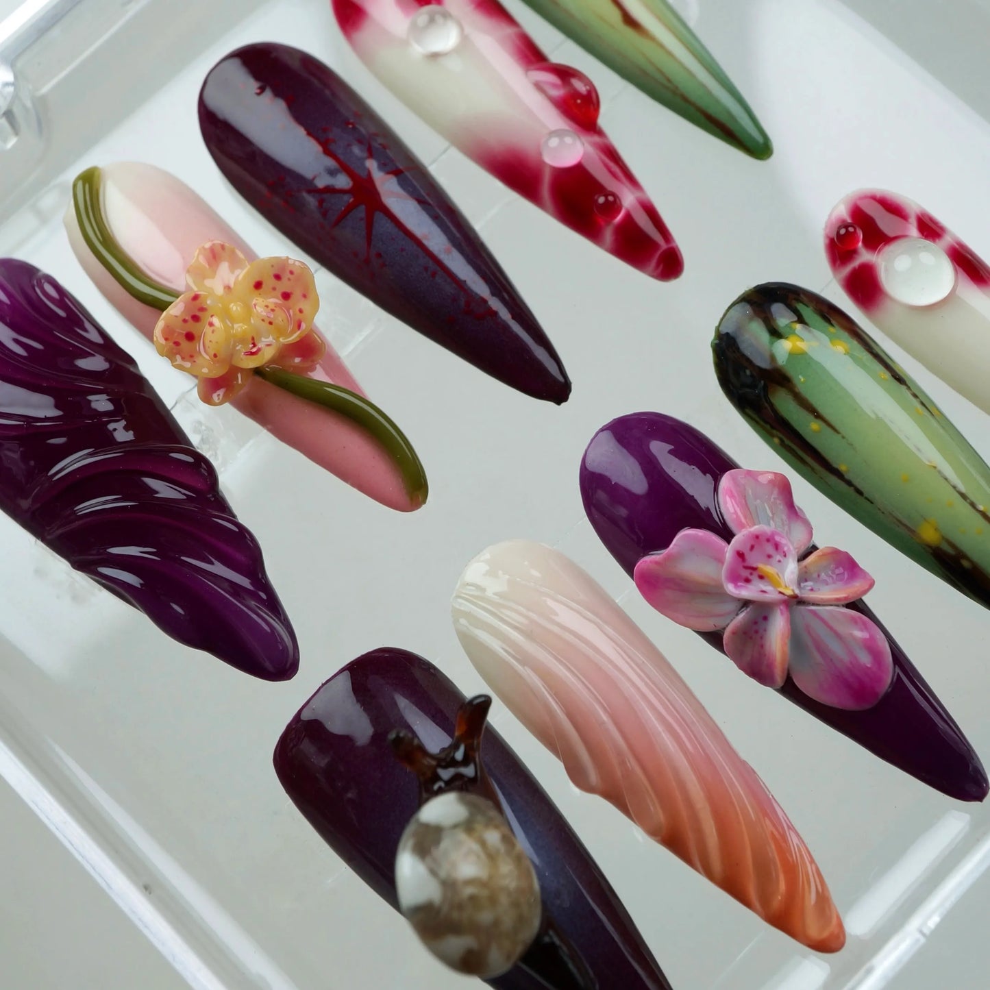 Artistic flower design nails with hand-painted leaves, orchids, and glossy gradients in a tropical garden palette