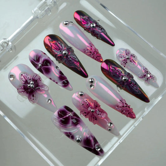 Shiny flower design nails in pink and violet tones, featuring delicate floral details and bold metallic accents