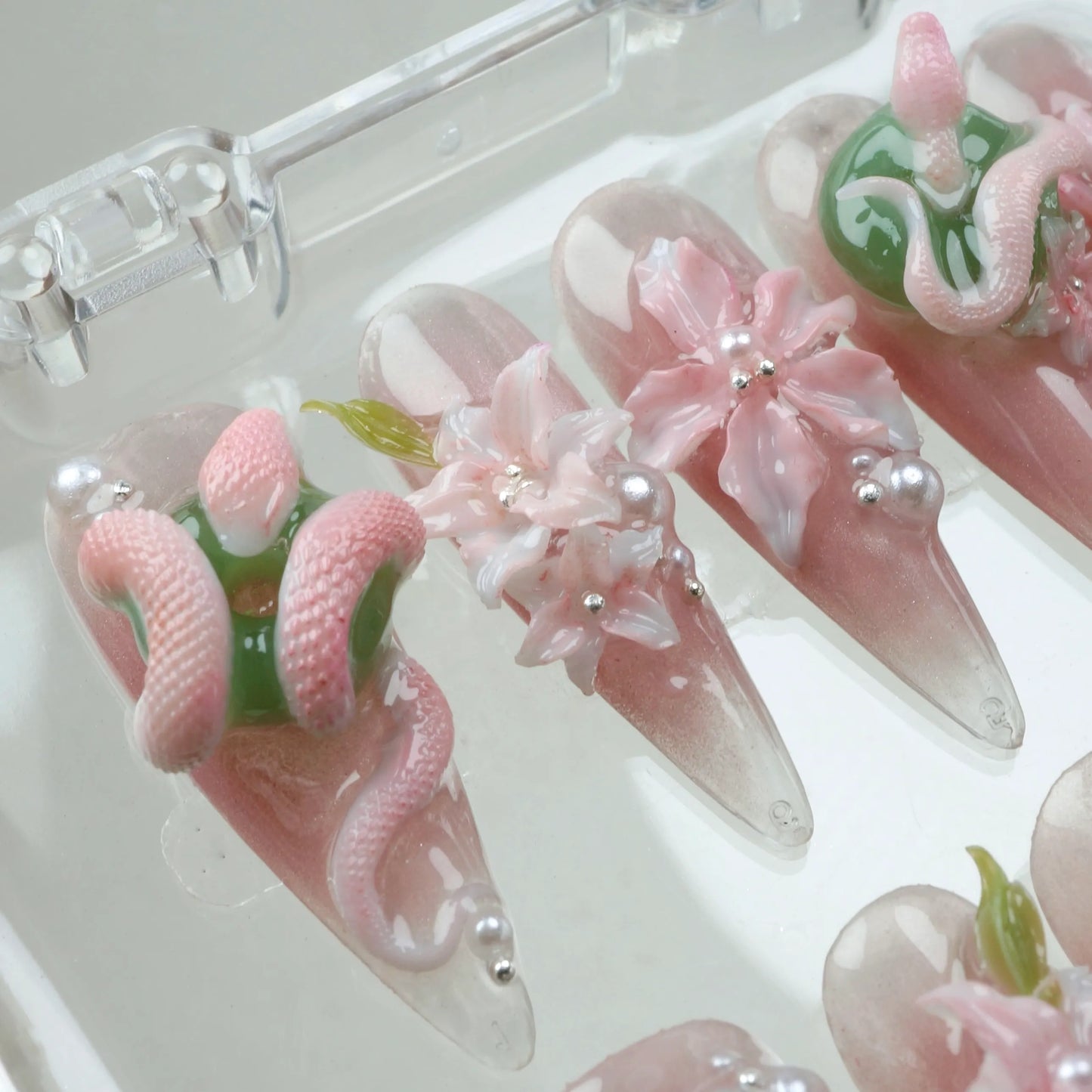 Artistic flower design nails combining translucent bases with sculpted snakes, delicate flowers, and pearls