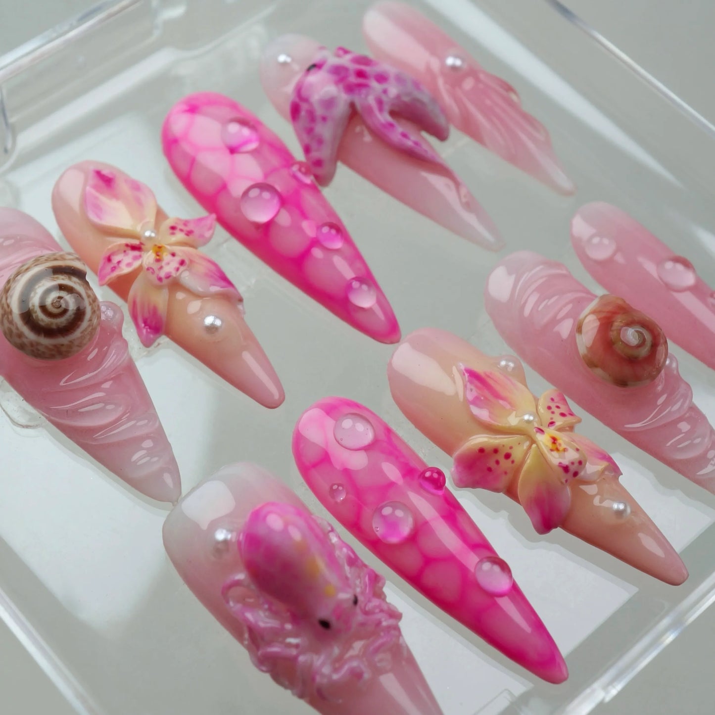Chic summer nails with a beachy pink theme, combining glossy finishes, shell accents, and subtle marine details.