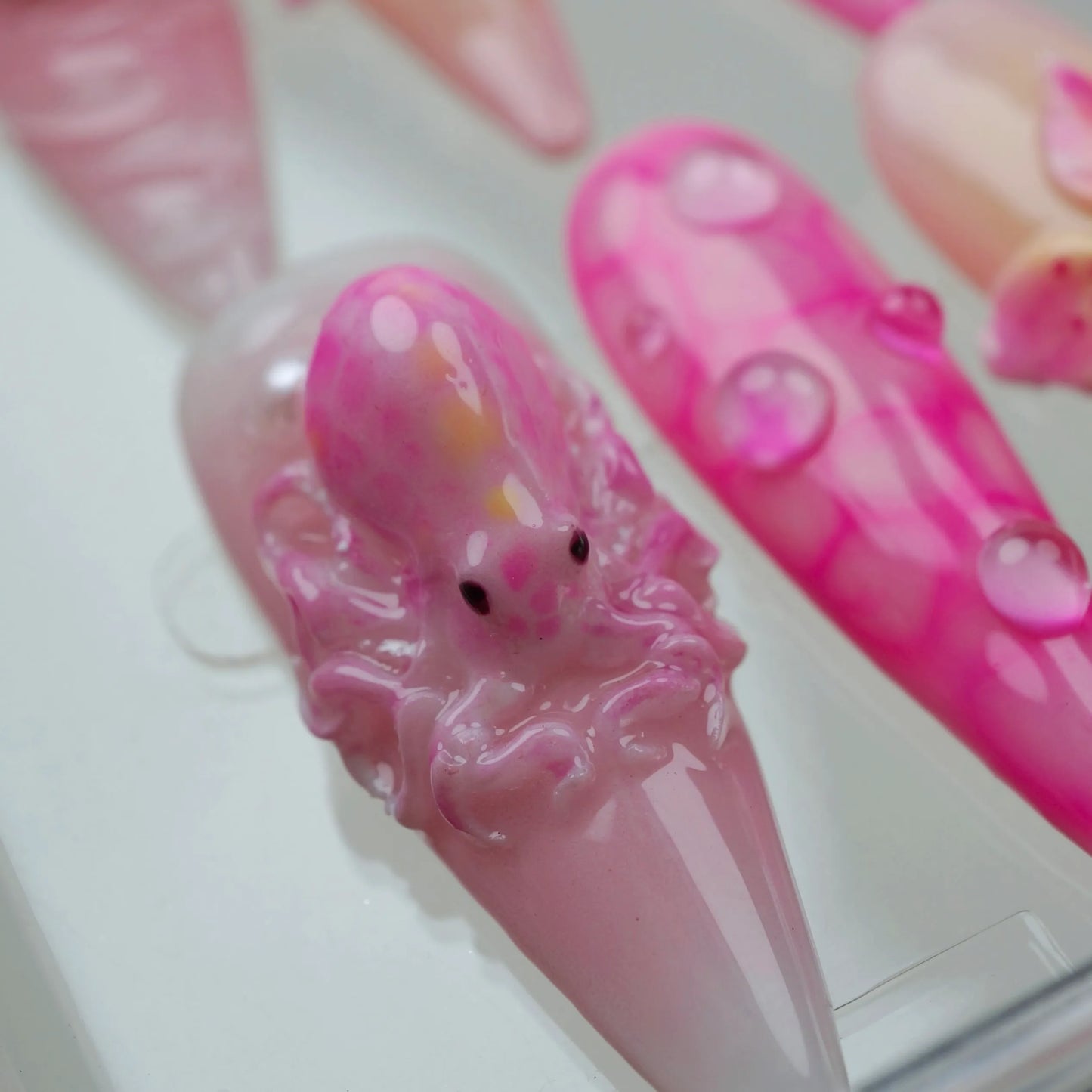 Whimsical summer nails with jellyfish designs, pearls, and a splash of bubble-like textures in pastel pink hues.