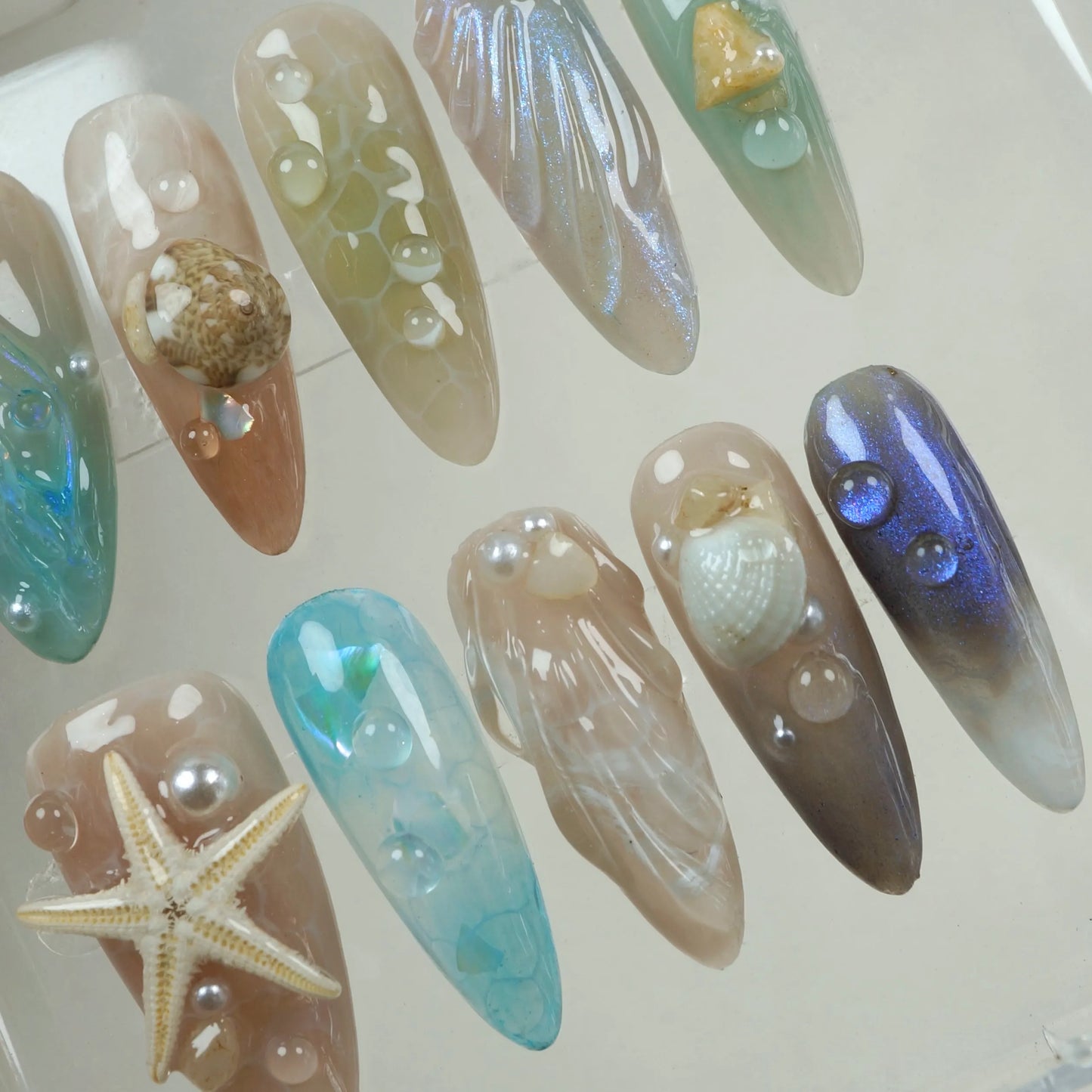 Elegant summer nails in cool blue and sandy beige tones, decorated with 3D seashells and underwater textures.