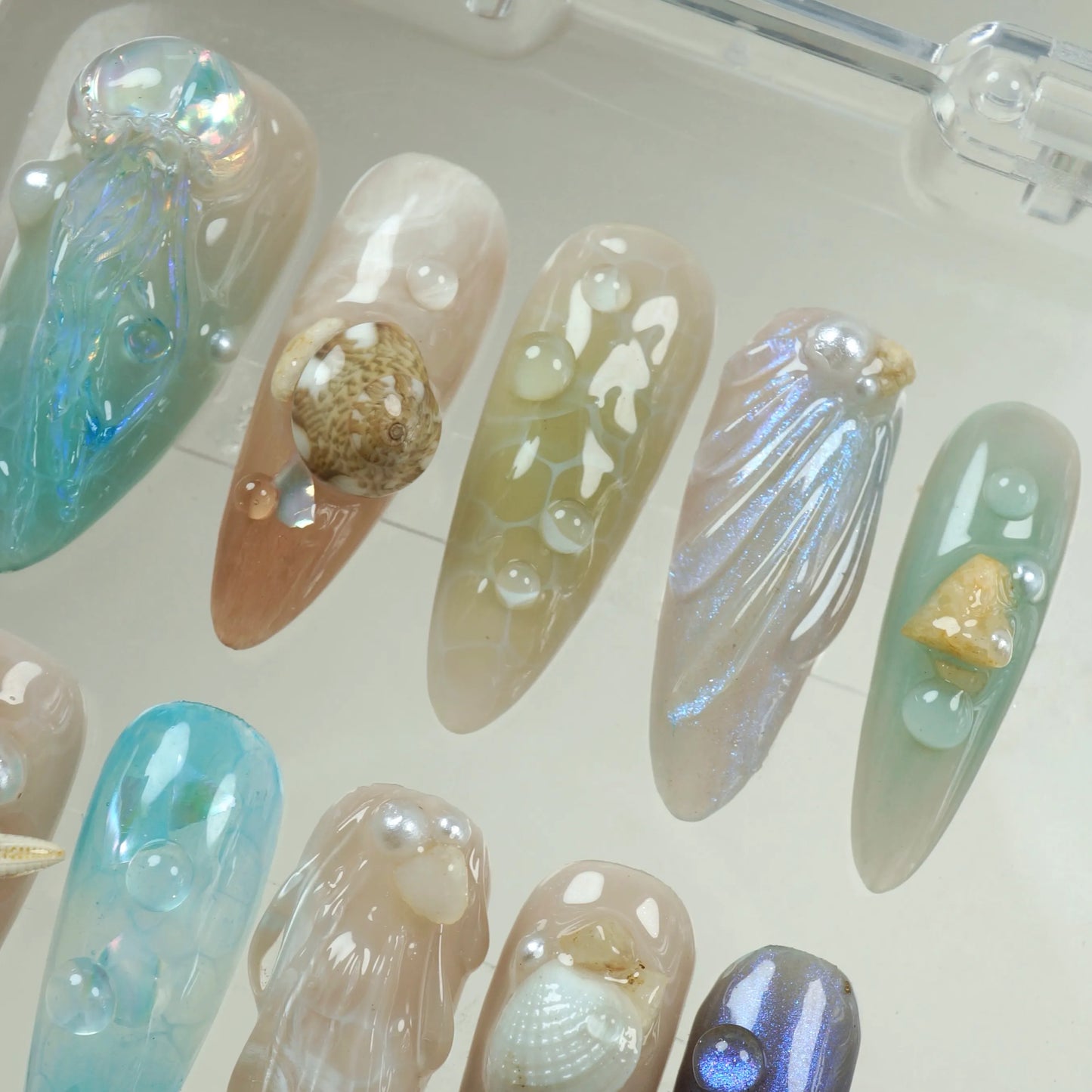 Under-the-sea themed summer nails with translucent blue tones, realistic seashells, and pearl accents.