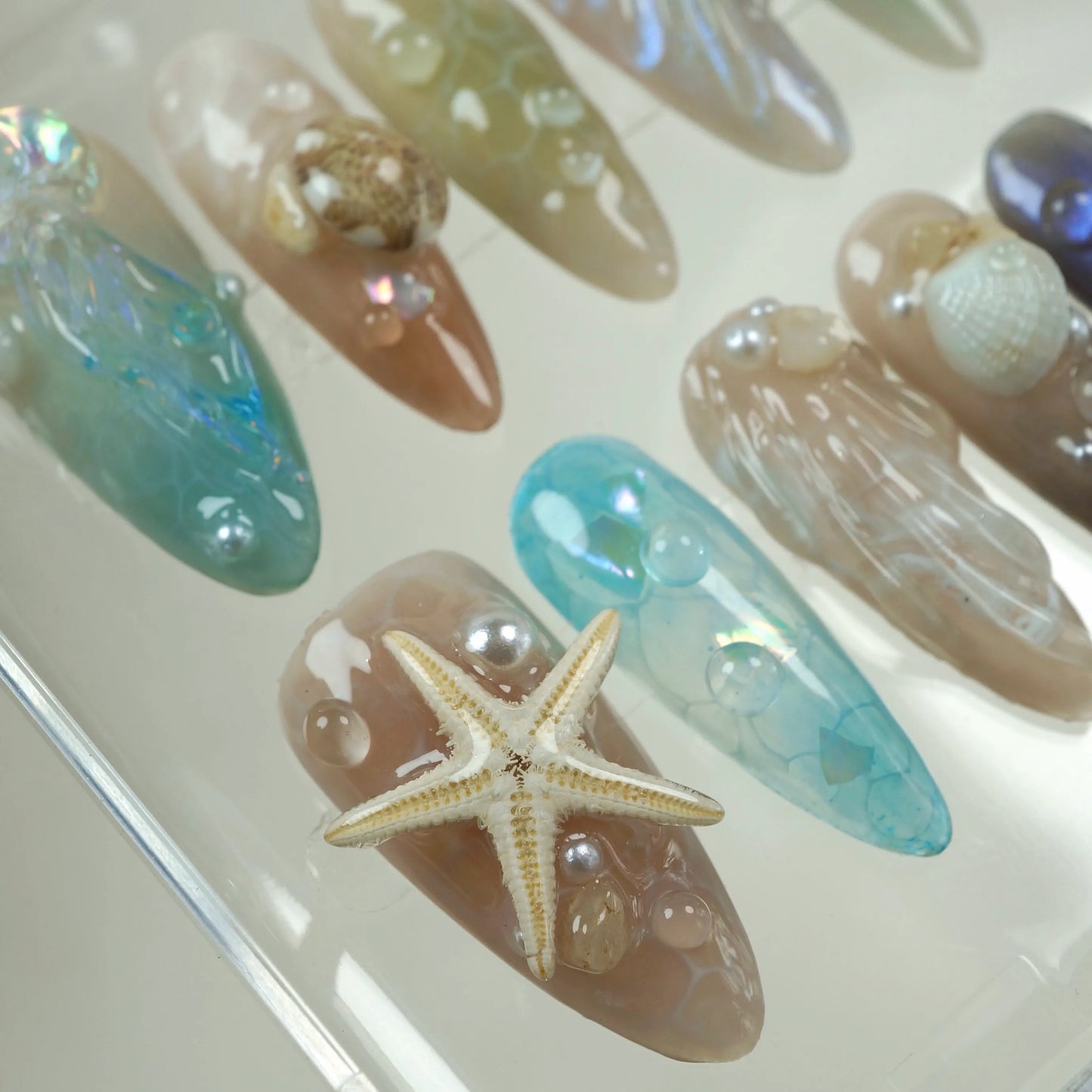 Creative summer nails inspired by the beach, featuring starfish, shells, and a glossy water droplet finish.