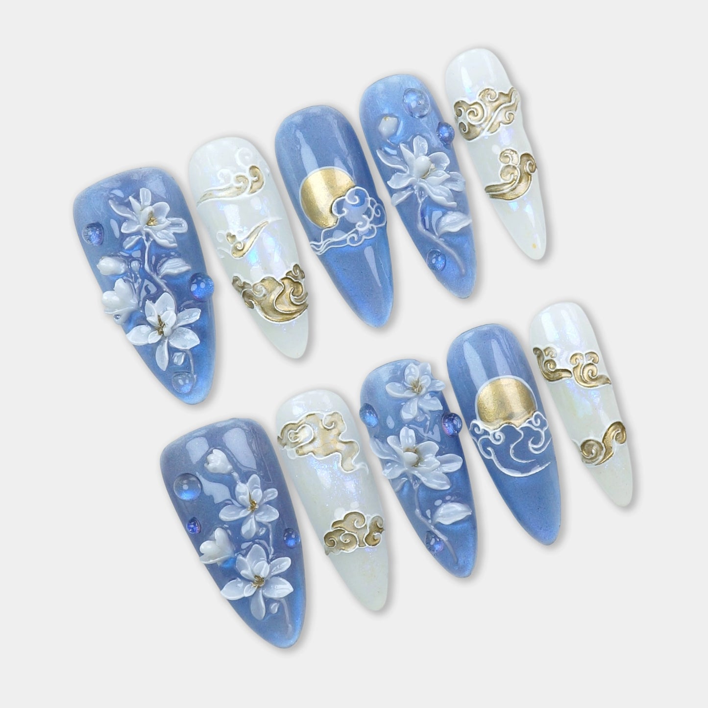 Press-on nails with hand-sculpted white florals, golden moon and cloud details, and soft blue and pearl shimmer base by Donailsart