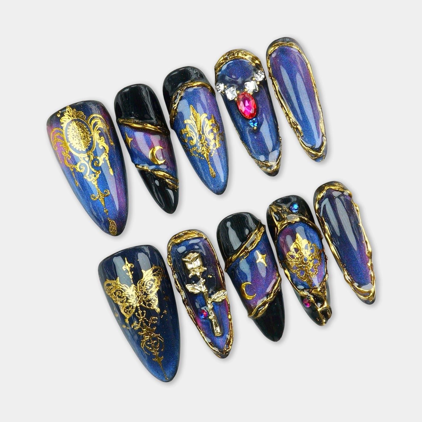 Press-on nails with deep galaxy blue base, gold foil baroque patterns, moon charms, and jeweled embellishments by Donailsart