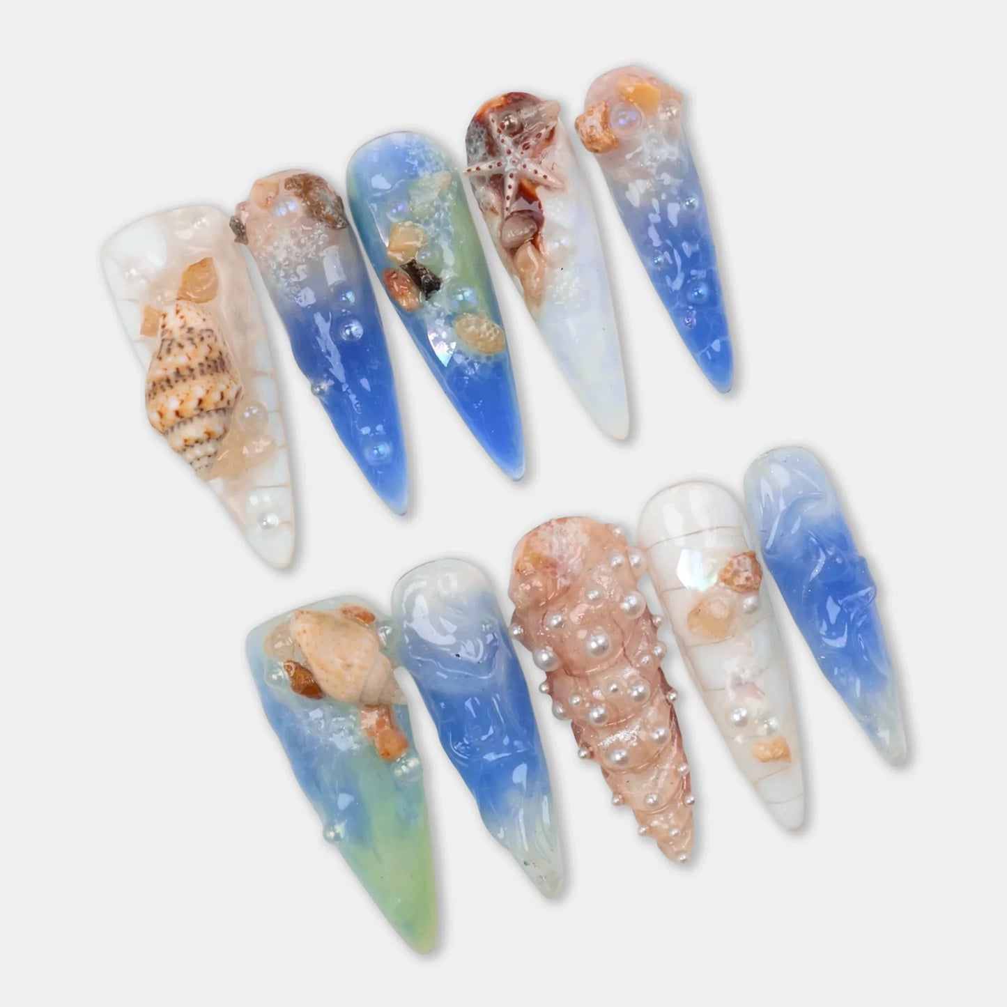 Ocean-inspired nail designs with seashells and blue gradient.