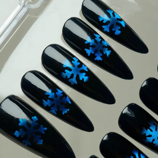 Glossy black press-on nails with metallic blue snowflake designs, inspired by a frosty winter night.