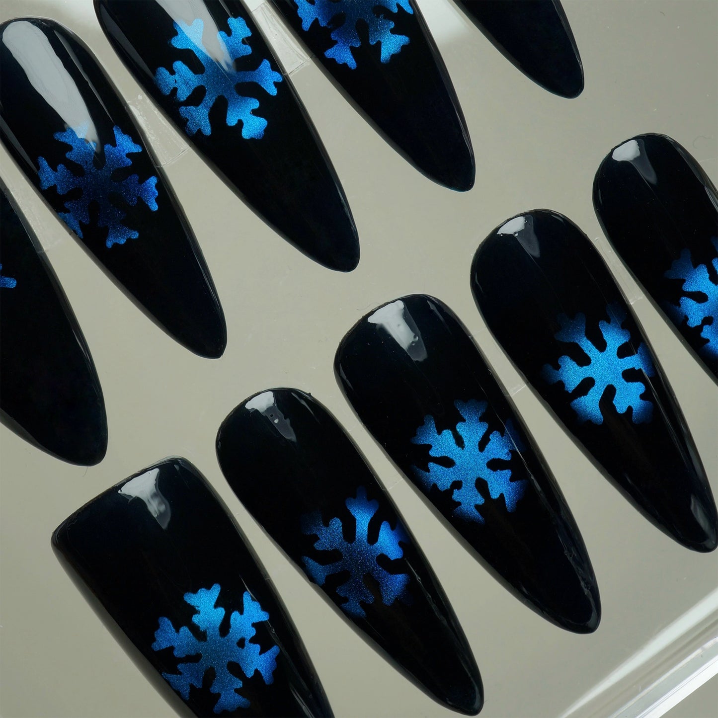 Black nails with blue snowflake designs on a neutral background