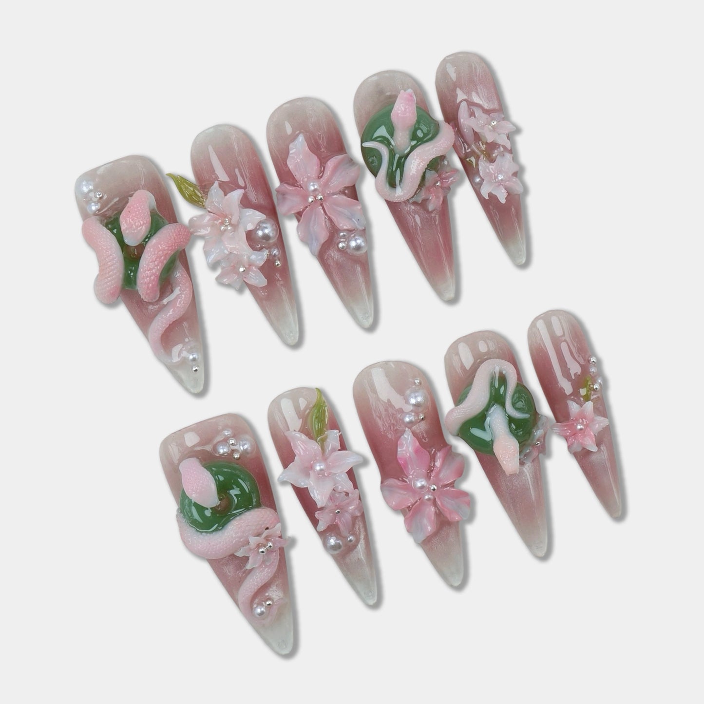 Soft pink flower design nails featuring 3D snakes, blossoms, and pearl accents for a whimsical and edgy style